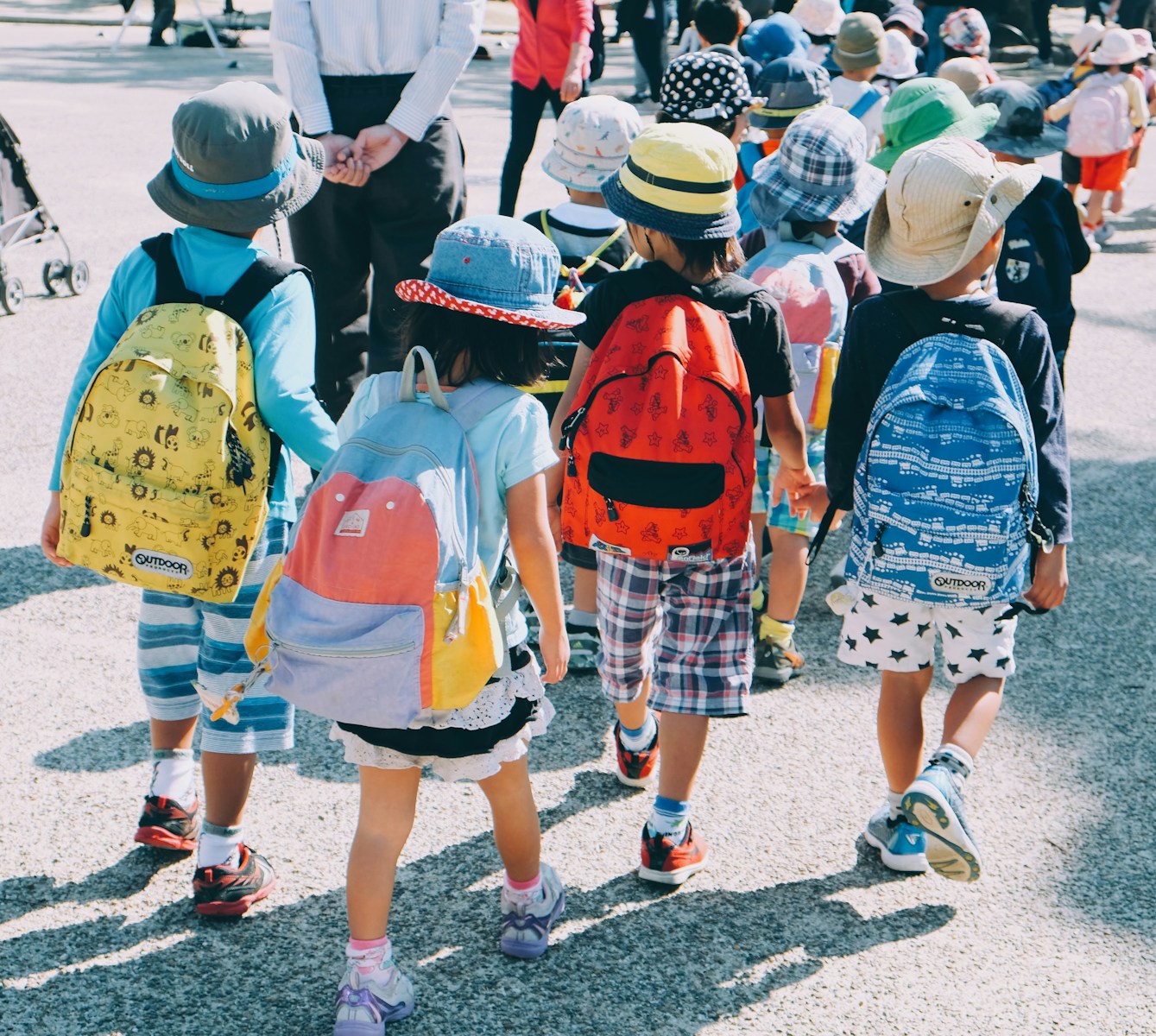 group of people wearing white and orange backpacks walking on gray concrete pavement during daytime, Die Grundschulzeit